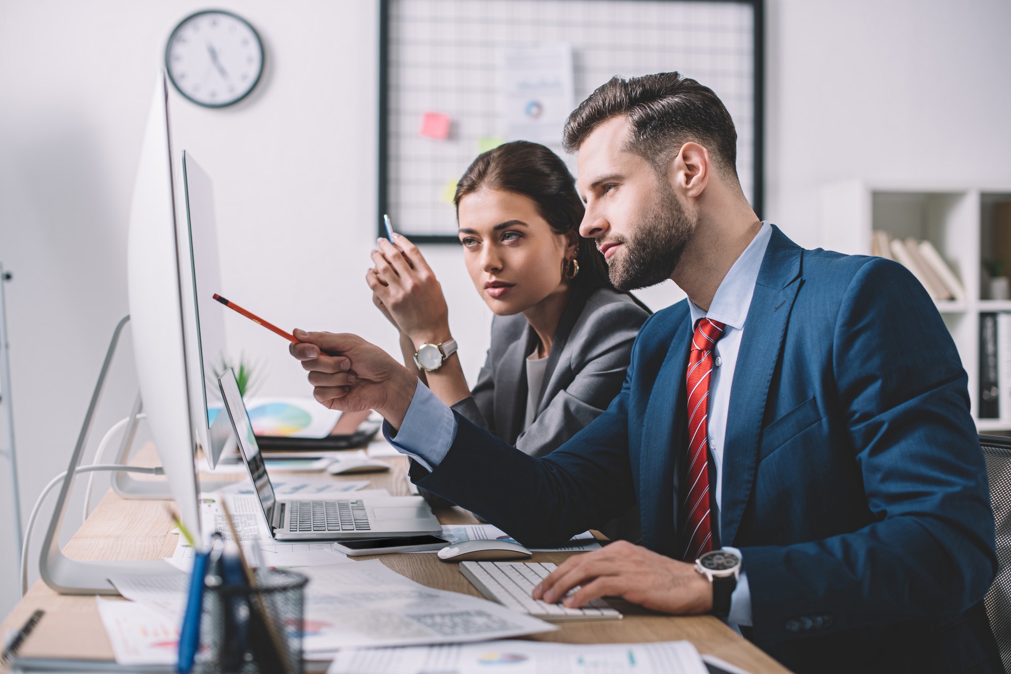 Side view of information security analyst pointing at computer monitor to colleague in office